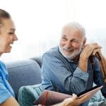 Healthcare worker speaking with an older man holding a walking stick in a bright home setting
