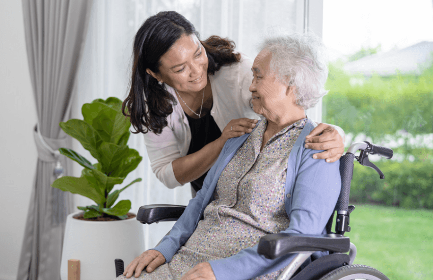 Woman leaning over smiling to older woman sitting in a wheelchair who is smiling back in relation to understanding the new aged care act.