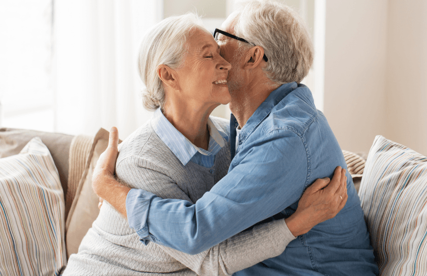 Older woman hugging and embracing and older man, while sitting on a lounge - in relation to caring for dementia.