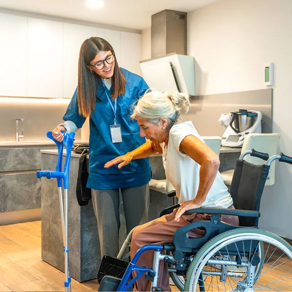 An elderly woman in a wheelchair receives assistance from a female caregiver.