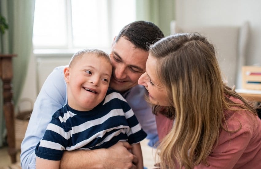 Family photo of mother and father embracing their disabled son in relation to in-home support